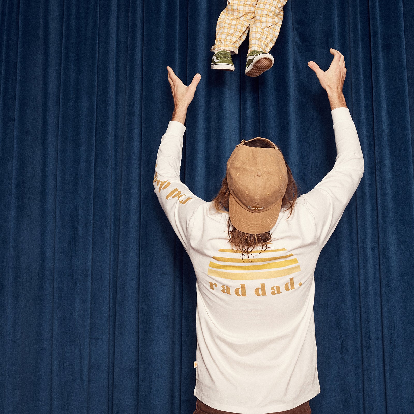 Person wearing a 'rad dad' shirt lifting a child against a blue curtain