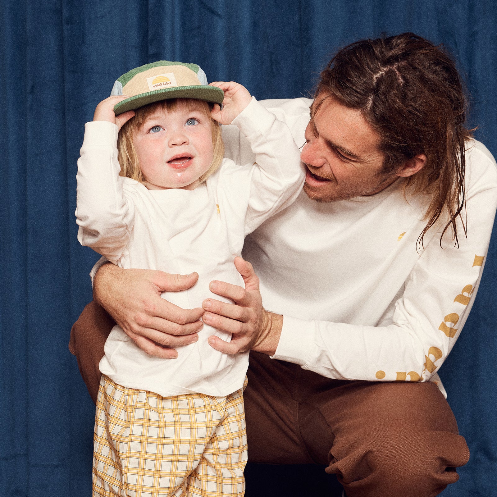 Man holding a child wearing a hat against a blue curtain background