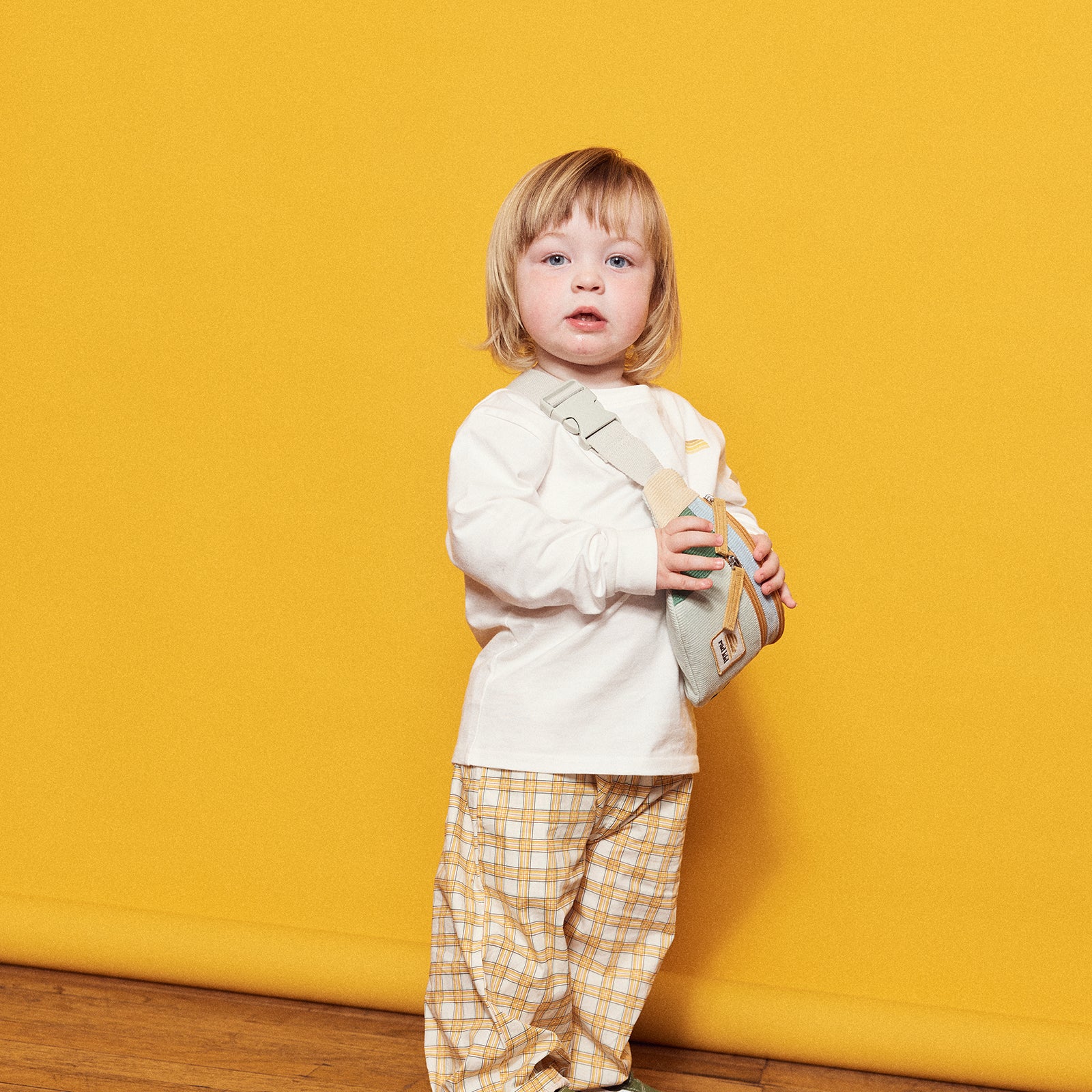 Child holding a belt bag across body wearing long sleeve rad kid tee