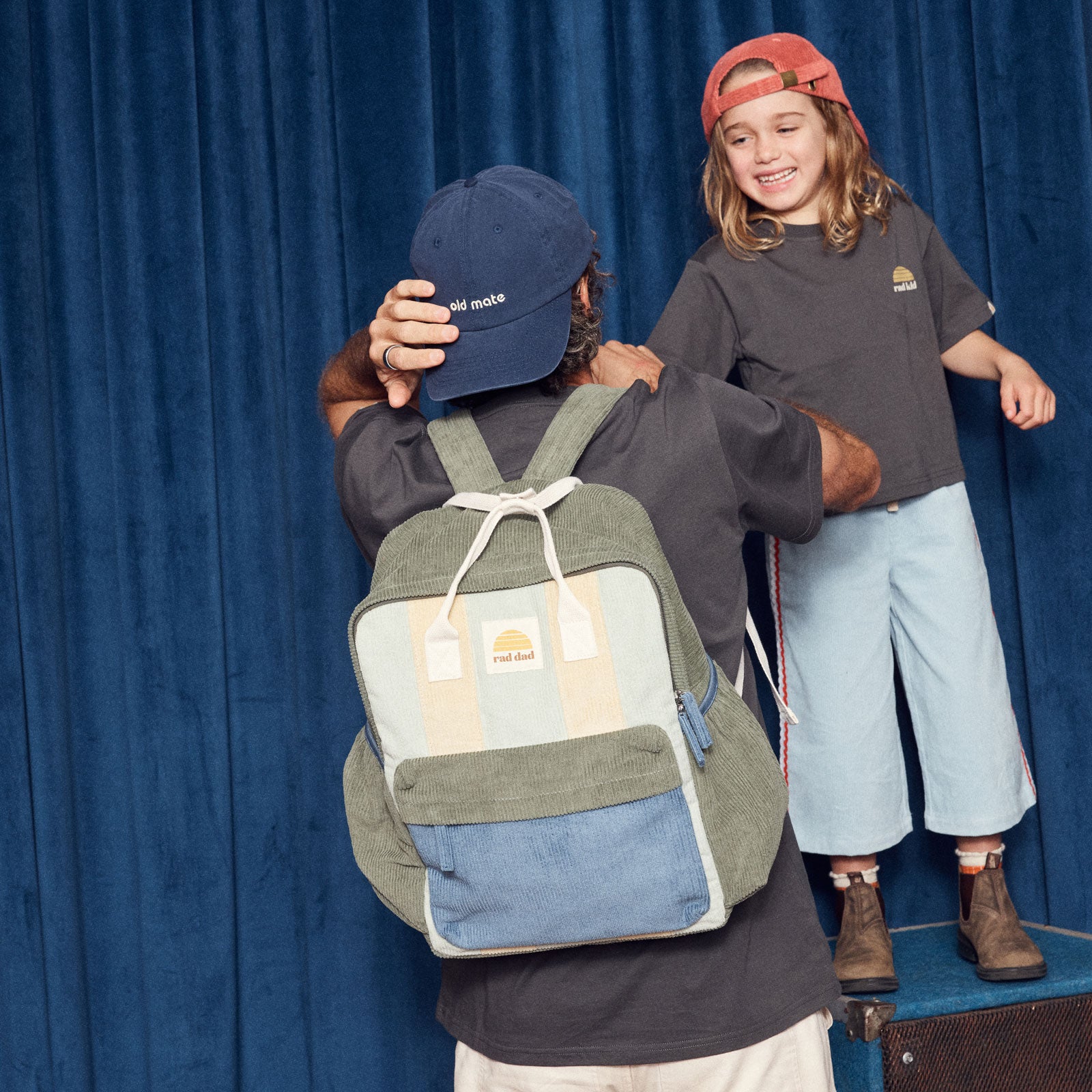 Person wearing a green and blue backpack wearing a navy 'old mate' cap