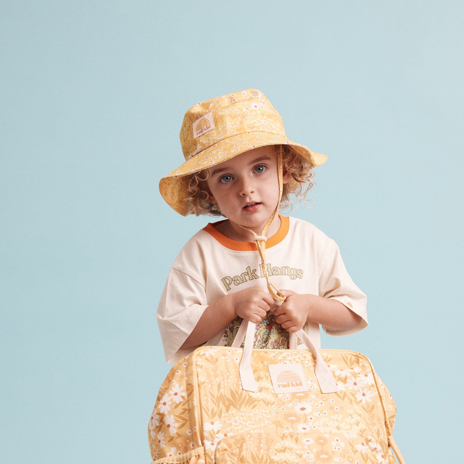 young child wearing he Rad Kid Buttercup print bucket hat holding a backpack in the same print.
