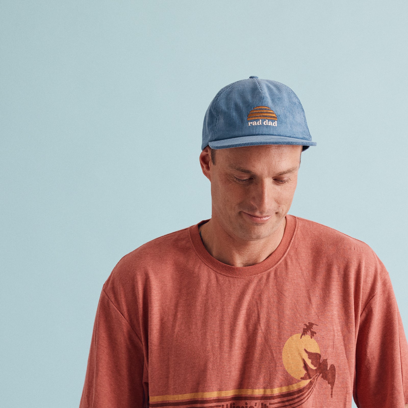 Man wearing Rad Dad corduroy pinch front flat peak cap in blue with Banabae sun logo on center front in yellow embroider with Rad Dad embroidered in off white underneath.
