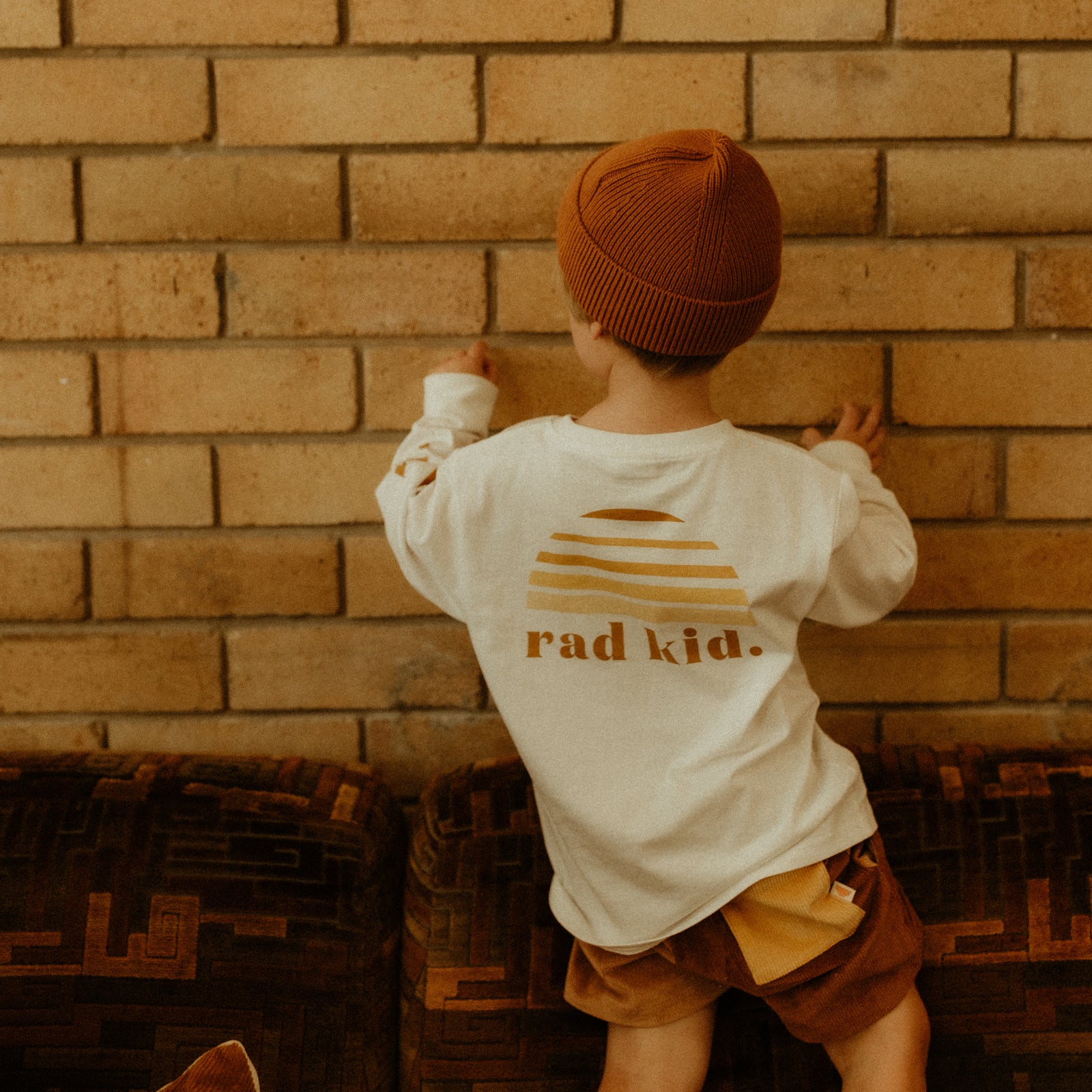 back view of a child wearing 'rad kid' long sleeve top and wearing a brown beanie