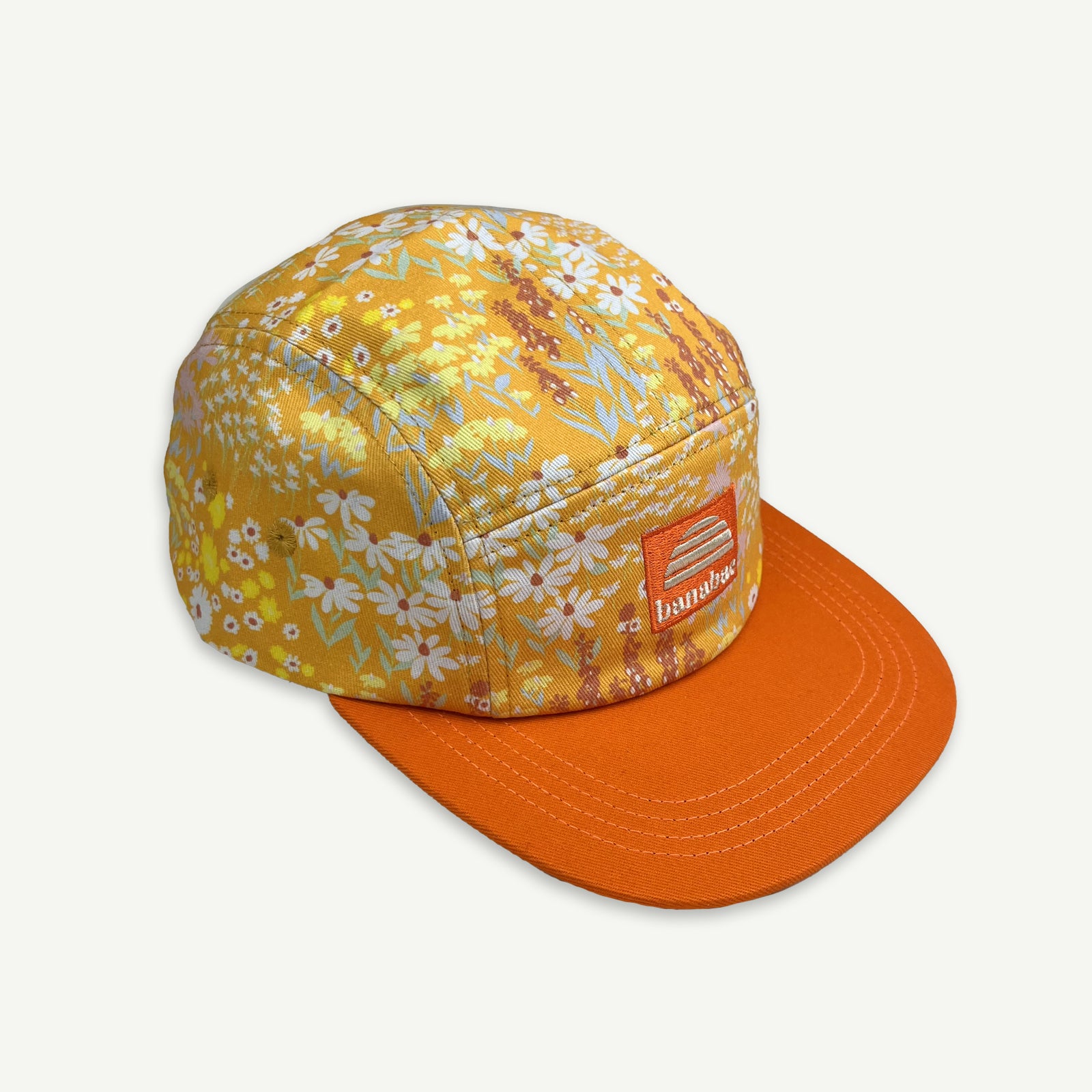 Off center view of 5 Panel cap in orange floral ditsy print with contrast orange peak and orange patch with the Banabae sun logo and Banabae embroidered in off white.