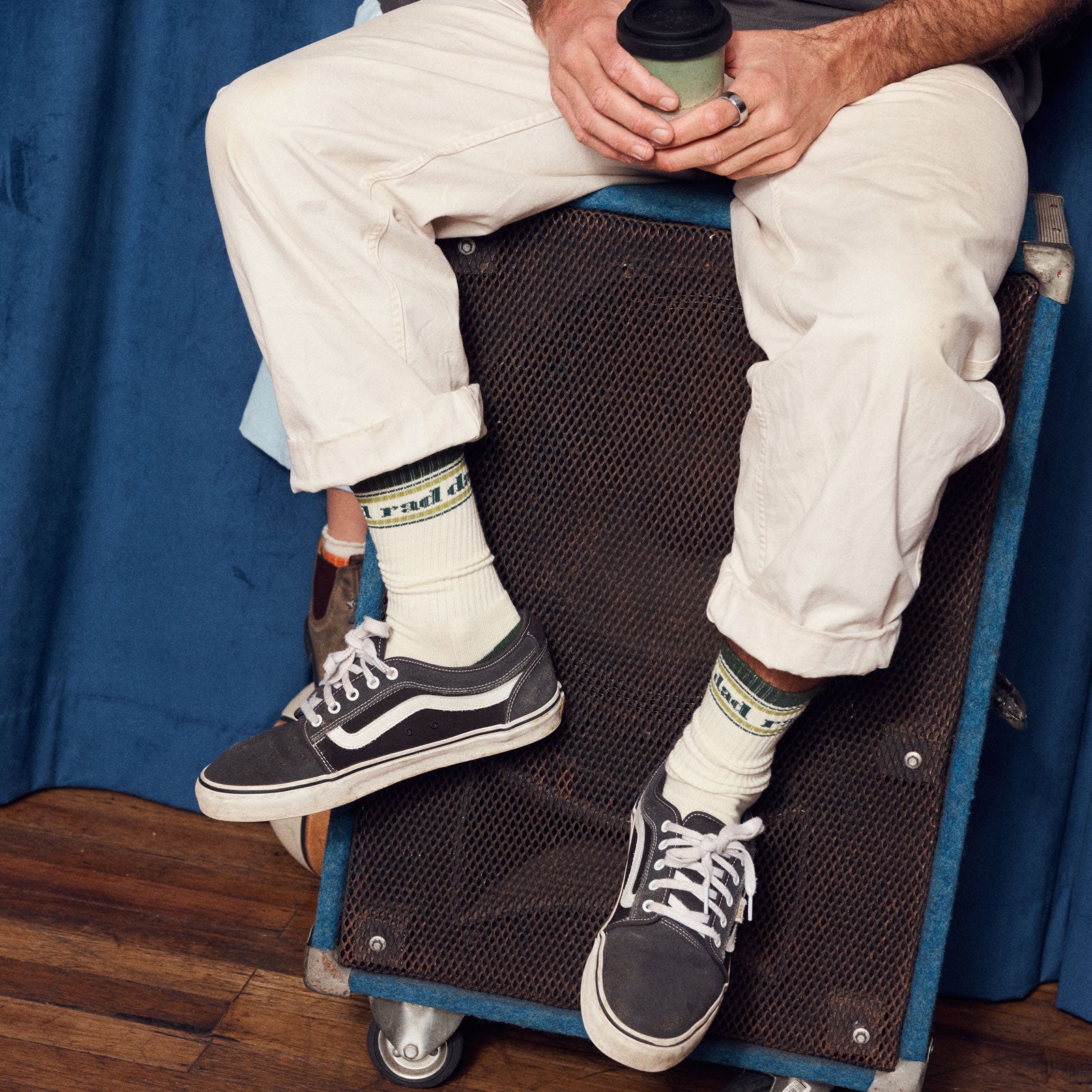 Person sitting on a speaker wearing white pants, black sneakers, and 'rad dad' socks.