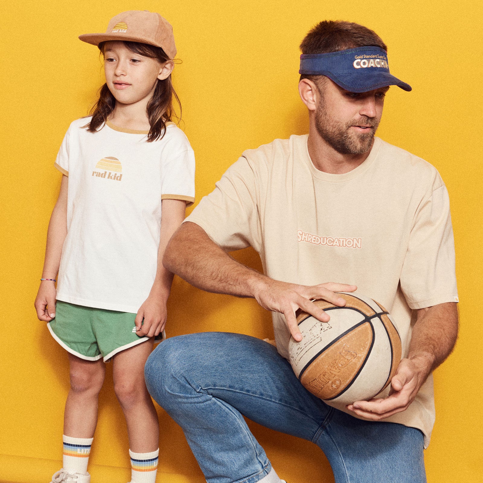 Man and young child standing against a yellow background, both wearing branded t-shirts.