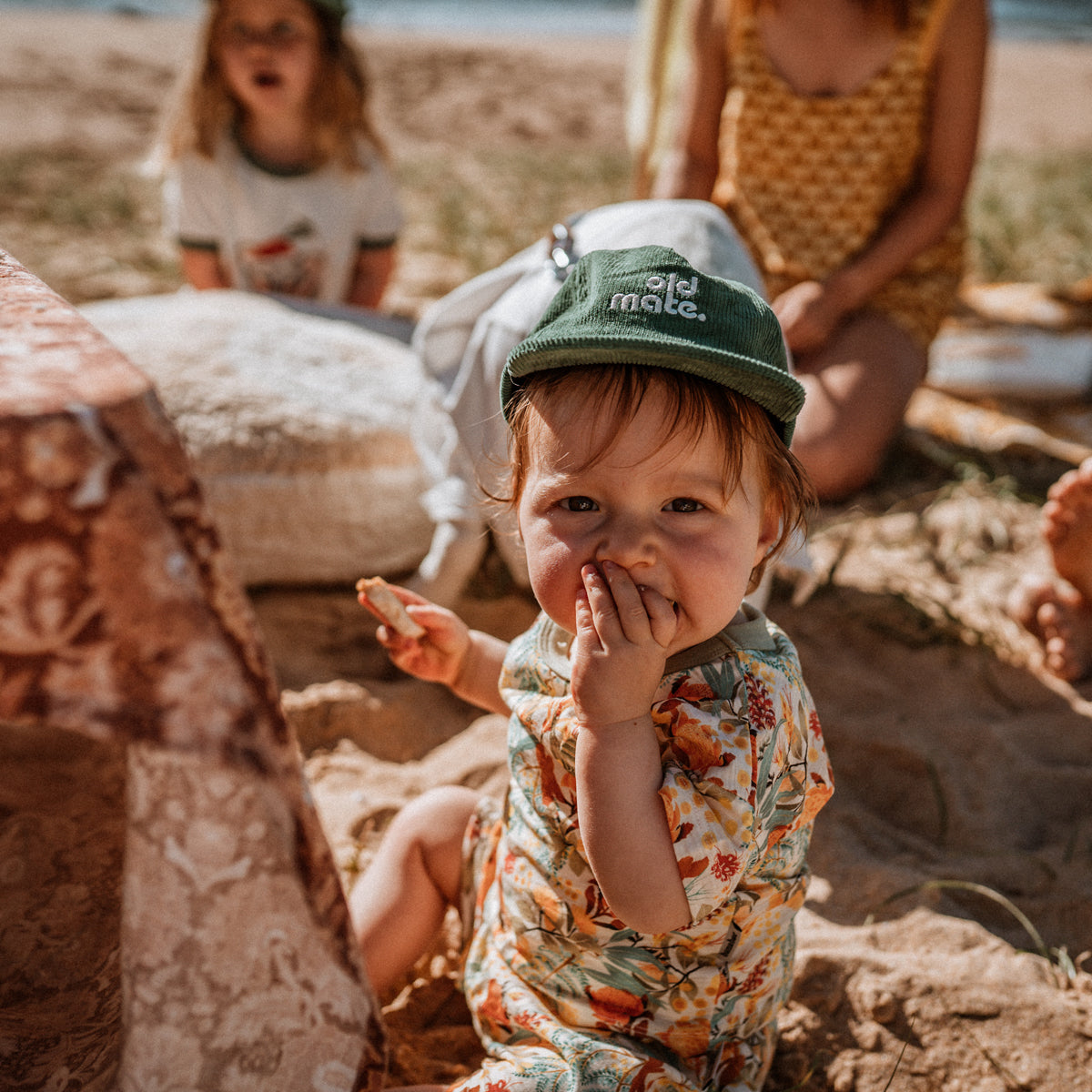 Lifestyle image of young child wearing Moss green corduroy pinch front cap with old mate embroidered on center front in contrast off white at the beach.
