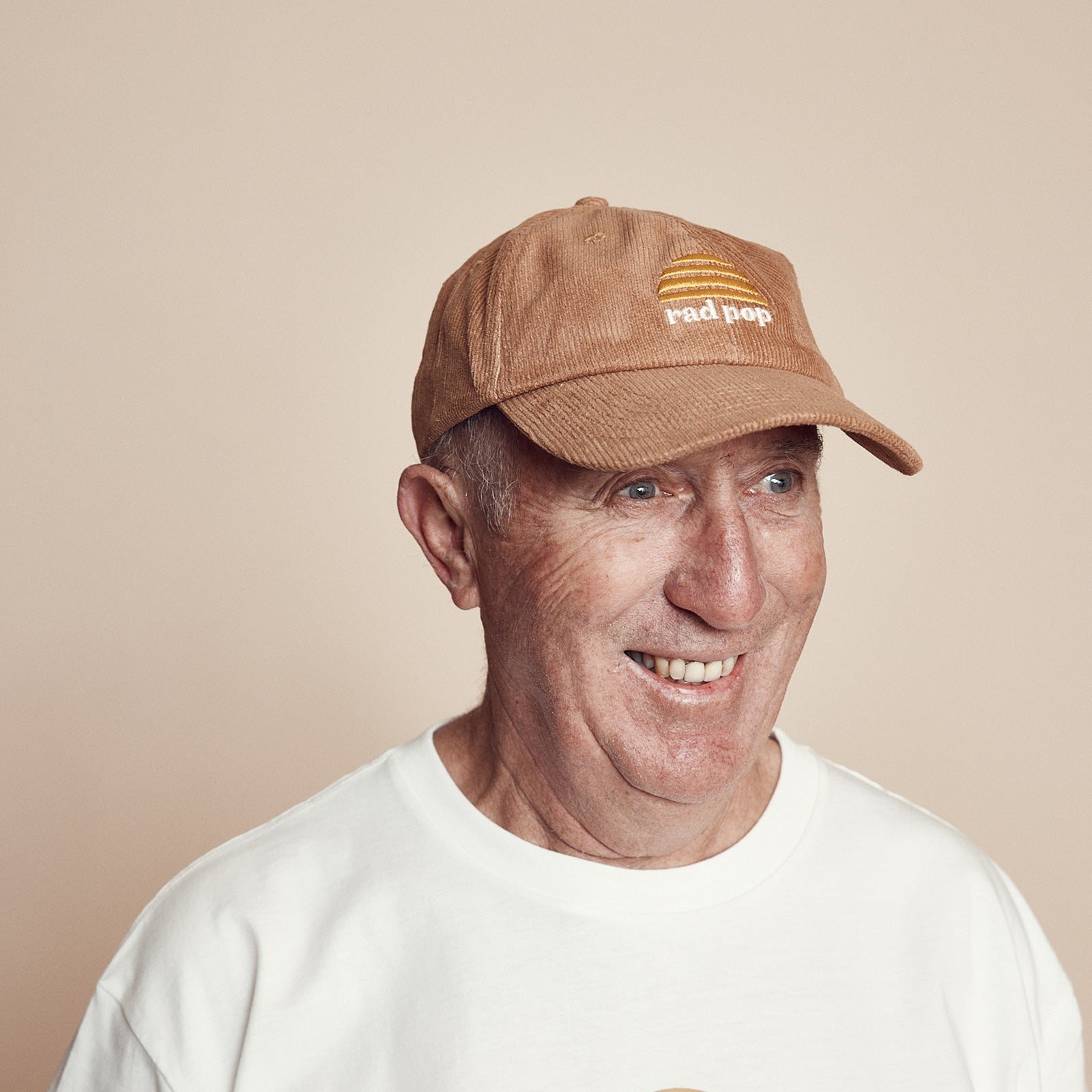 Off center image of smiling gentleman wearing Rad pop corduroy flat peaked cap with Banabae sun logo in yellow embroidered on center front with Rad Pop underneath in off white.