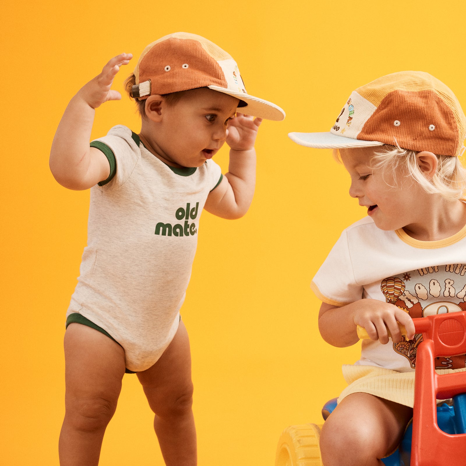 Image of happy one year old standing up wearing a cap and natural grey marled onesie with contrast green ringer bind at sleeve, neckline and hemp. Old Mate in green printed at center front.