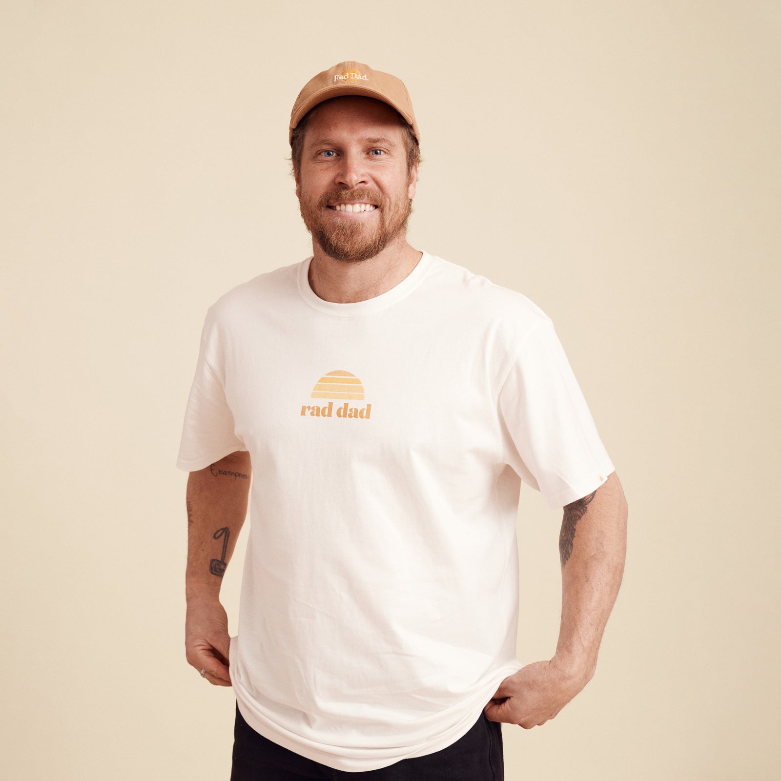 Man wearing a white t-shirt with 'rad dad' text and a brown cap on a beige background