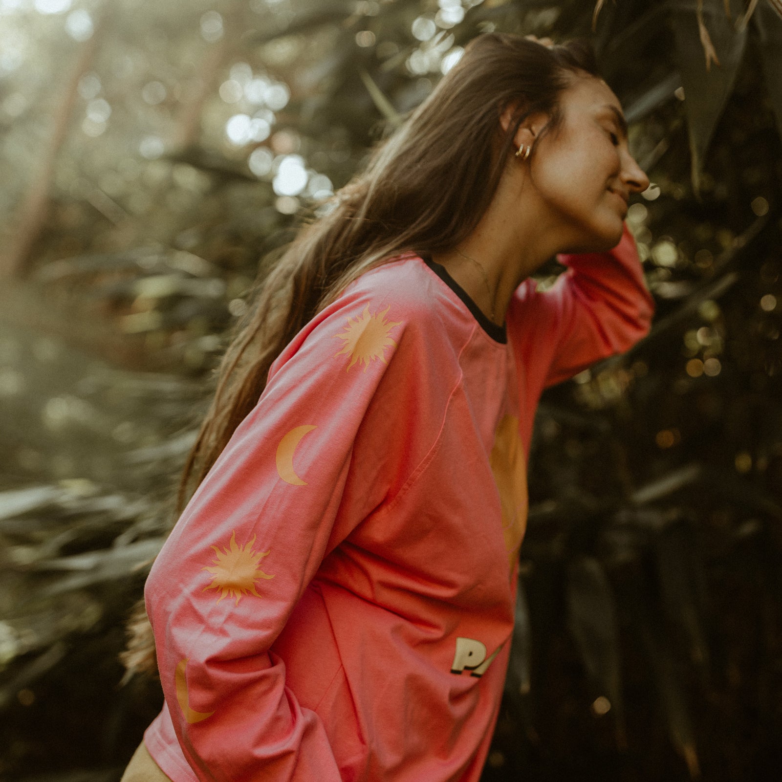 Woman wearing a pink 'Parlife' long sleeve tee with a sun graphic in a natural setting