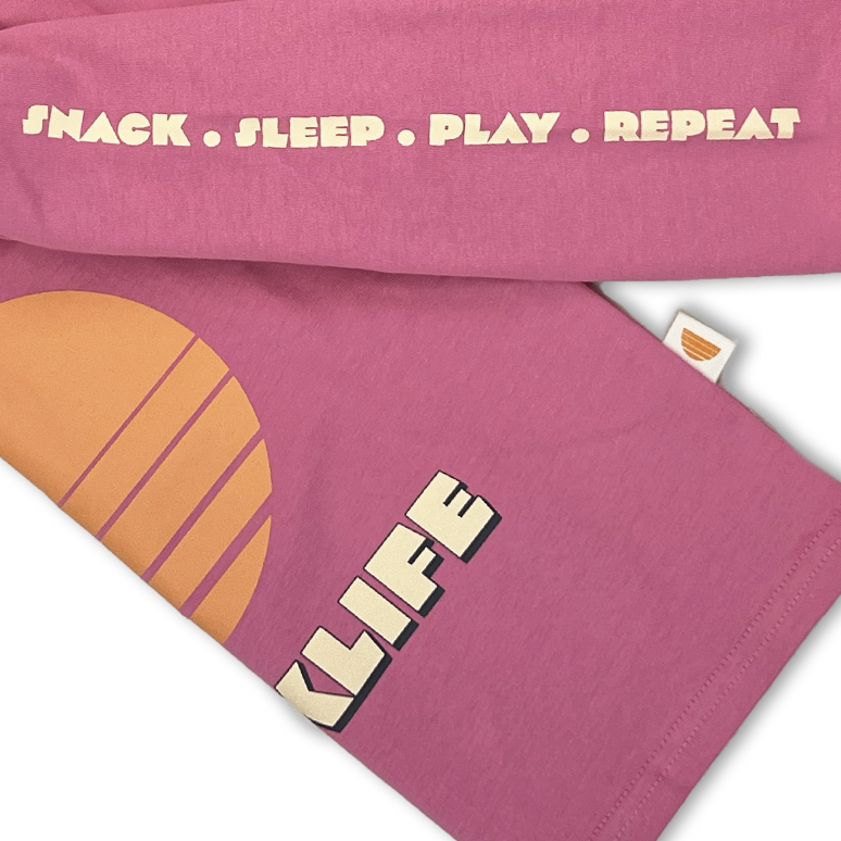 Pink long sleeve tee with text and a sun graphic on a white background